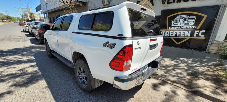 White pickup truck with canopy at a vehicle dealership lot under sunny skies
