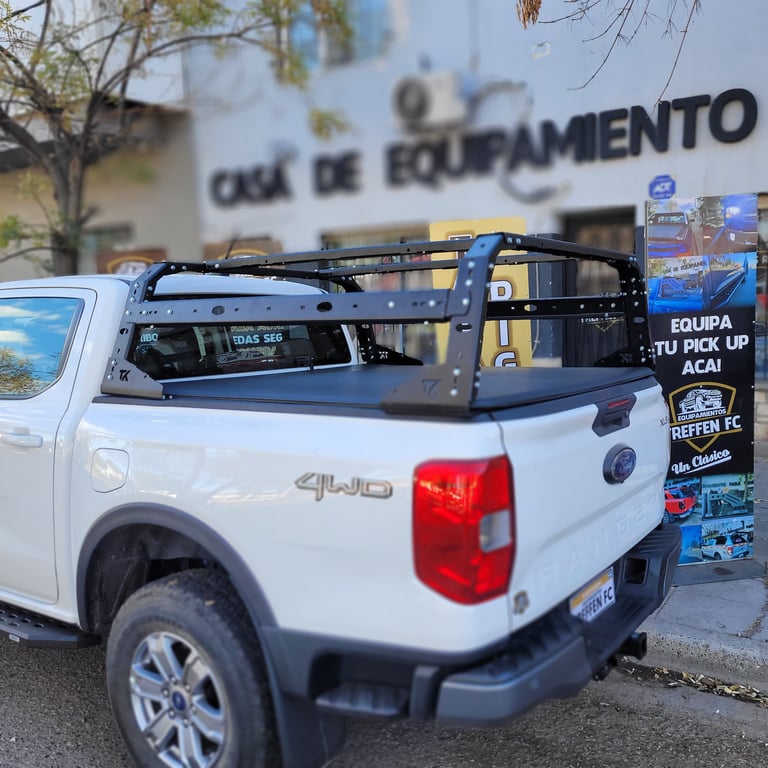 White pickup truck with roof rack and black toolbox parked outside an equipment shop