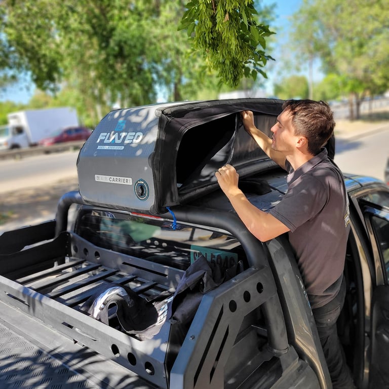 Man installing a black tonneau cover on the bed of a black pickup truck in a sunny residential area