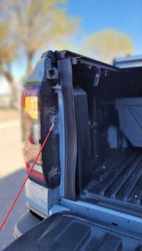 Close-up of an open truck bed tonneau cover with red taillights visible, parked outdoors on a sunny day