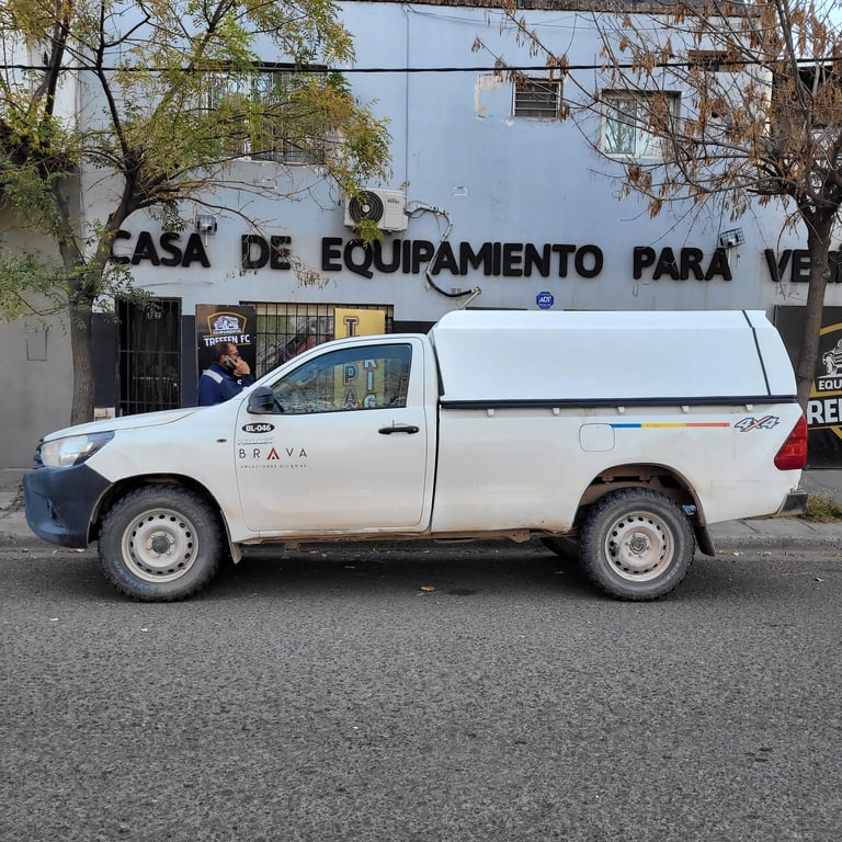 White pickup truck parked on street in front of building with Portuguese signage and bare trees