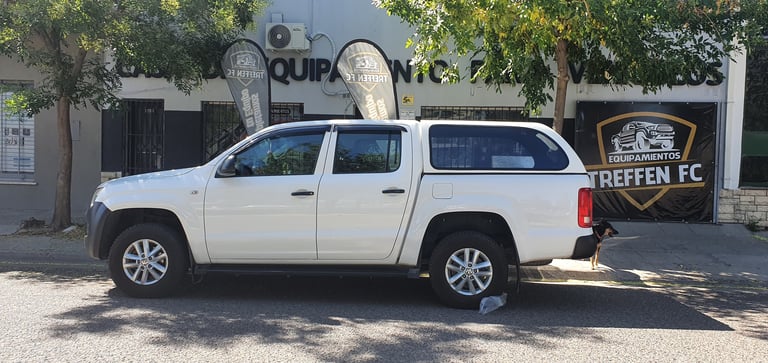 White pickup truck with canopy parked on street in front of storefronts with trees in background