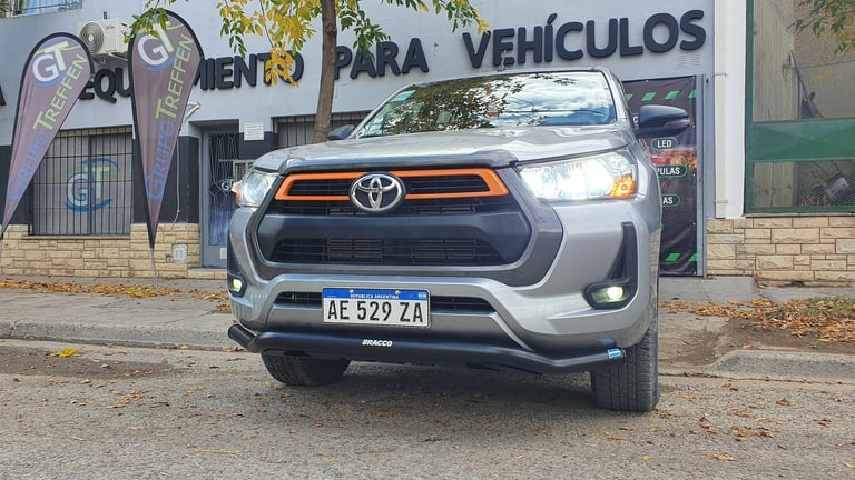 Silver Toyota pickup truck with orange trim parked in front of a vehicles dealership storefront