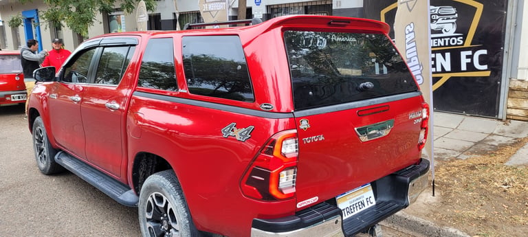 Red Toyota pickup truck parked on a street, rear view showing dual cab body style