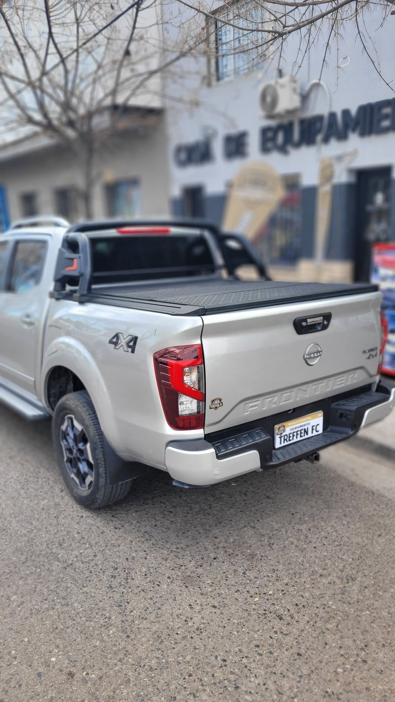 White Nissan pickup truck with tonneau cover parked in front of a building with bare trees