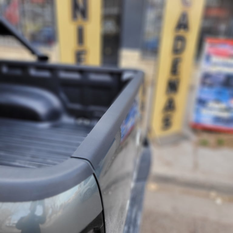 Close-up of a truck bed cover edge with yellow vertical signs blurred in background at dealership