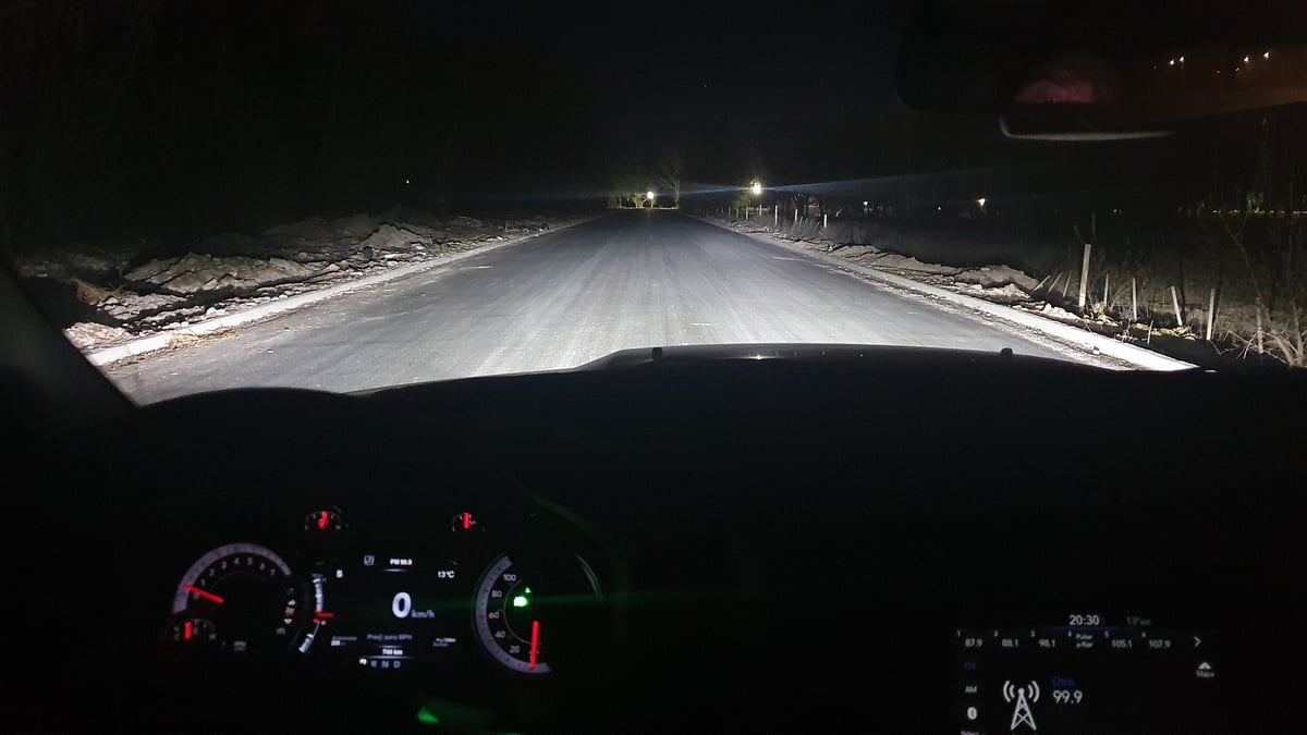 Dashboard view of a car driving on a snow-covered road at night with headlights illuminating the path ahead