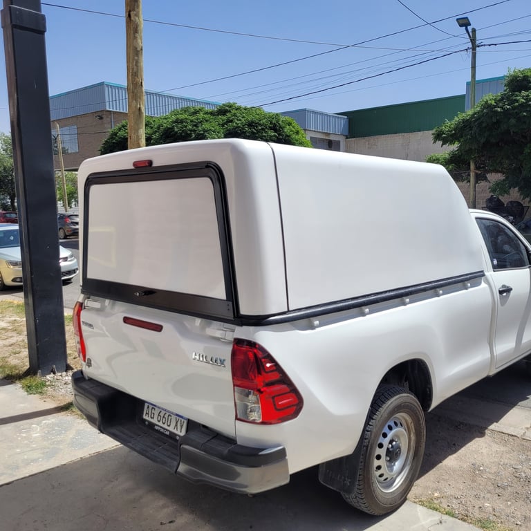 White pickup truck with white cargo canopy parked on street with utility poles and buildings in background