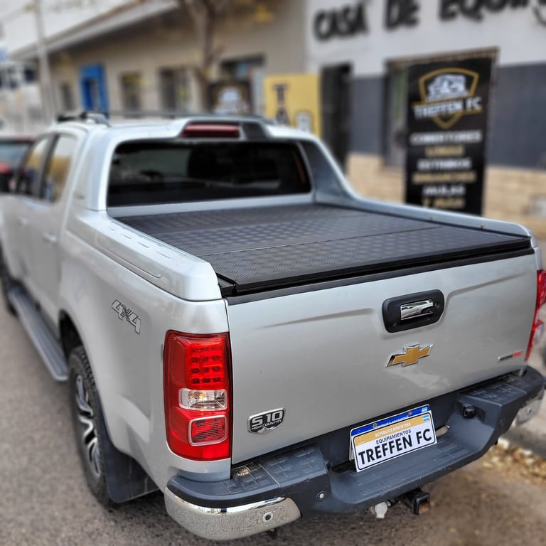 White Chevrolet pickup truck with black tonneau cover bed, shown from rear angle with buildings in background