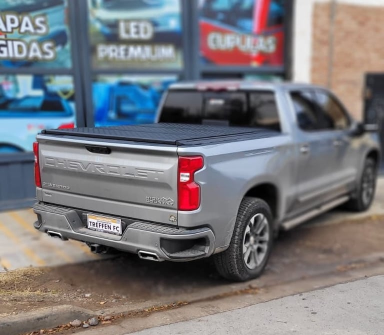 Silver Chevrolet Silverado pickup truck model displayed outdoors with automotive shop in blurred background