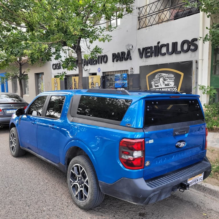 Blue Ford pickup truck parked outside a Spanish repair shop building with signage