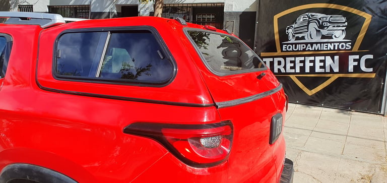 Bright red compact vehicle parked in front of a shop with Treffen FC logo sign